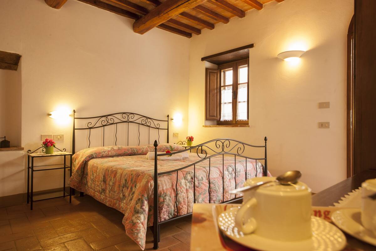 A bedroom with a bed, bedside tables, a window, and a table with a teapot and cups.