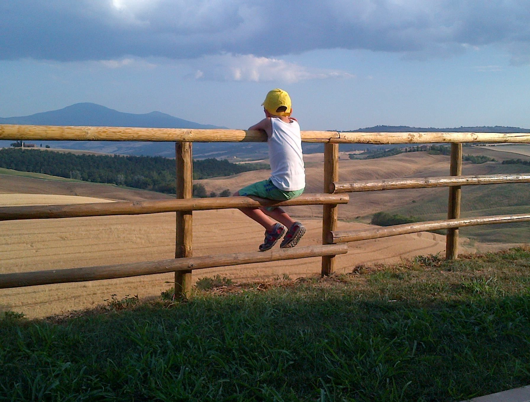 Una persona trepando una valla de madera con vistas a un paisaje rural con campos y colinas al lejano.