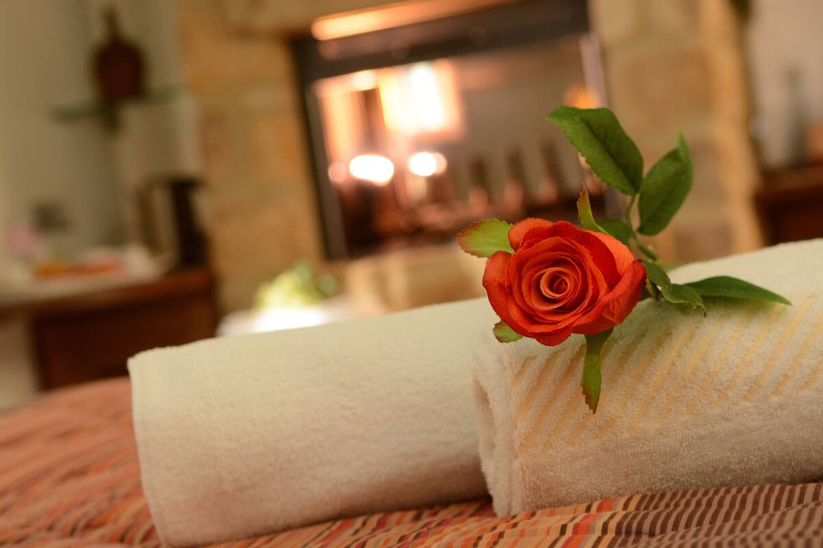 A neatly folded white towel with a red rose on it, placed on a striped bedspread.
