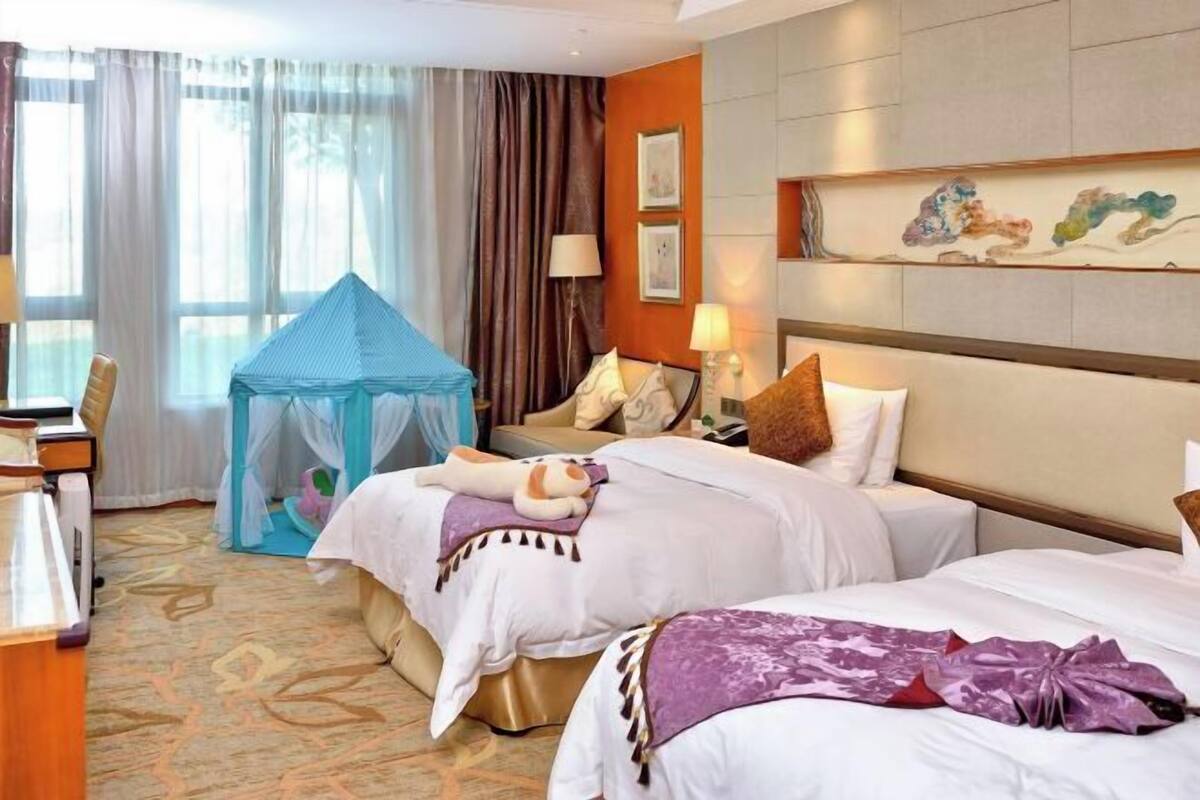 Une chambre d’hôtel avec deux lits, un bureau, une chaise, une petite tente et des œuvres d’art accrochées au mur.
