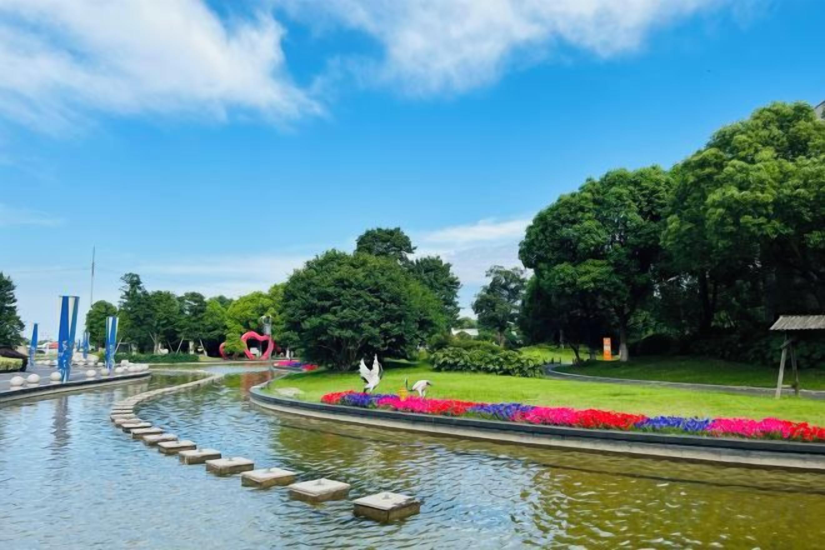 Un parque con fuente de agua, escalones de piedra y parterres florales.