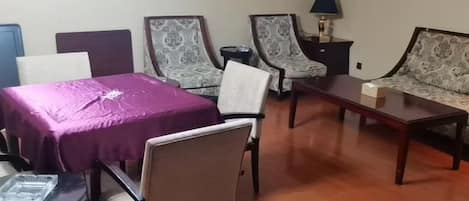 A room with a table, two armchairs, a sofa, and a lamp.