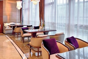 A modern hotel lobby with a dining area, large windows, and a marble floor.
