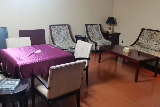 A room with a purple table, two patterned armchairs, a sofa, a small round table, and a lamp on a nightstand.