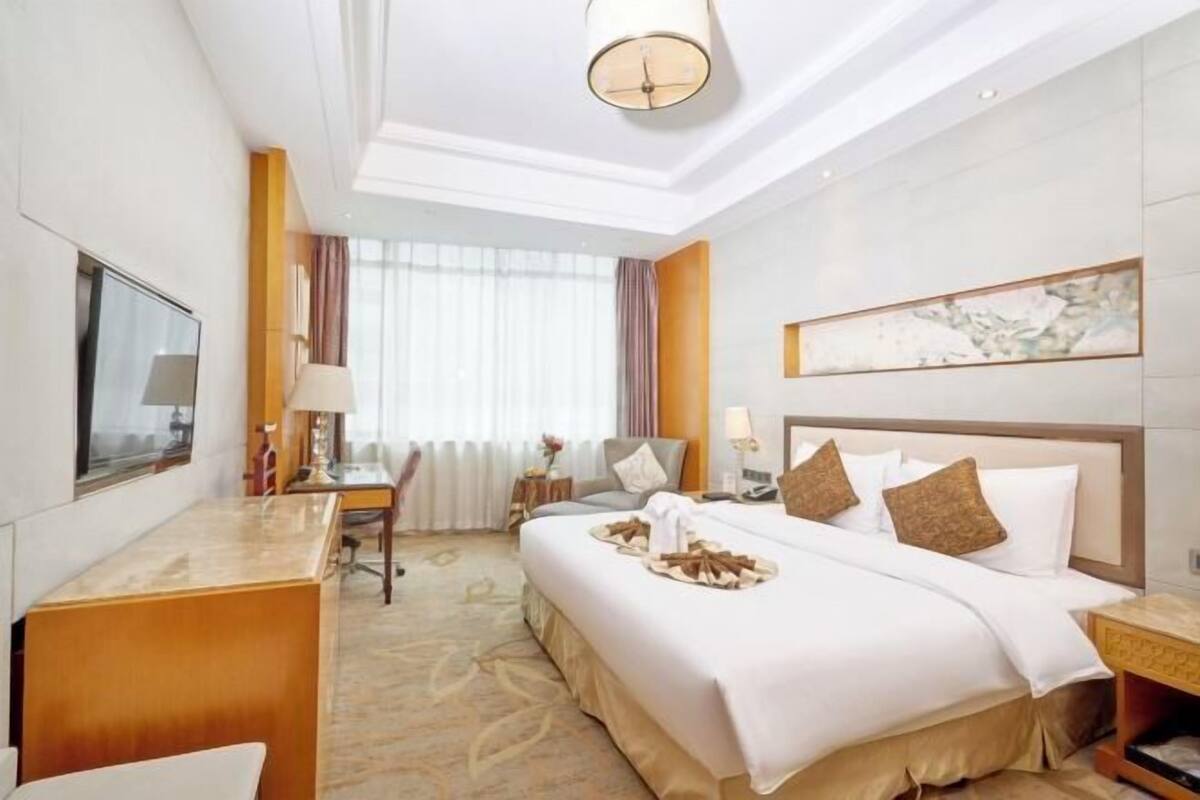 Une chambre d’hôtel avec un lit, une table de chevet, une lampe et une grande fenêtre avec des rideaux.
