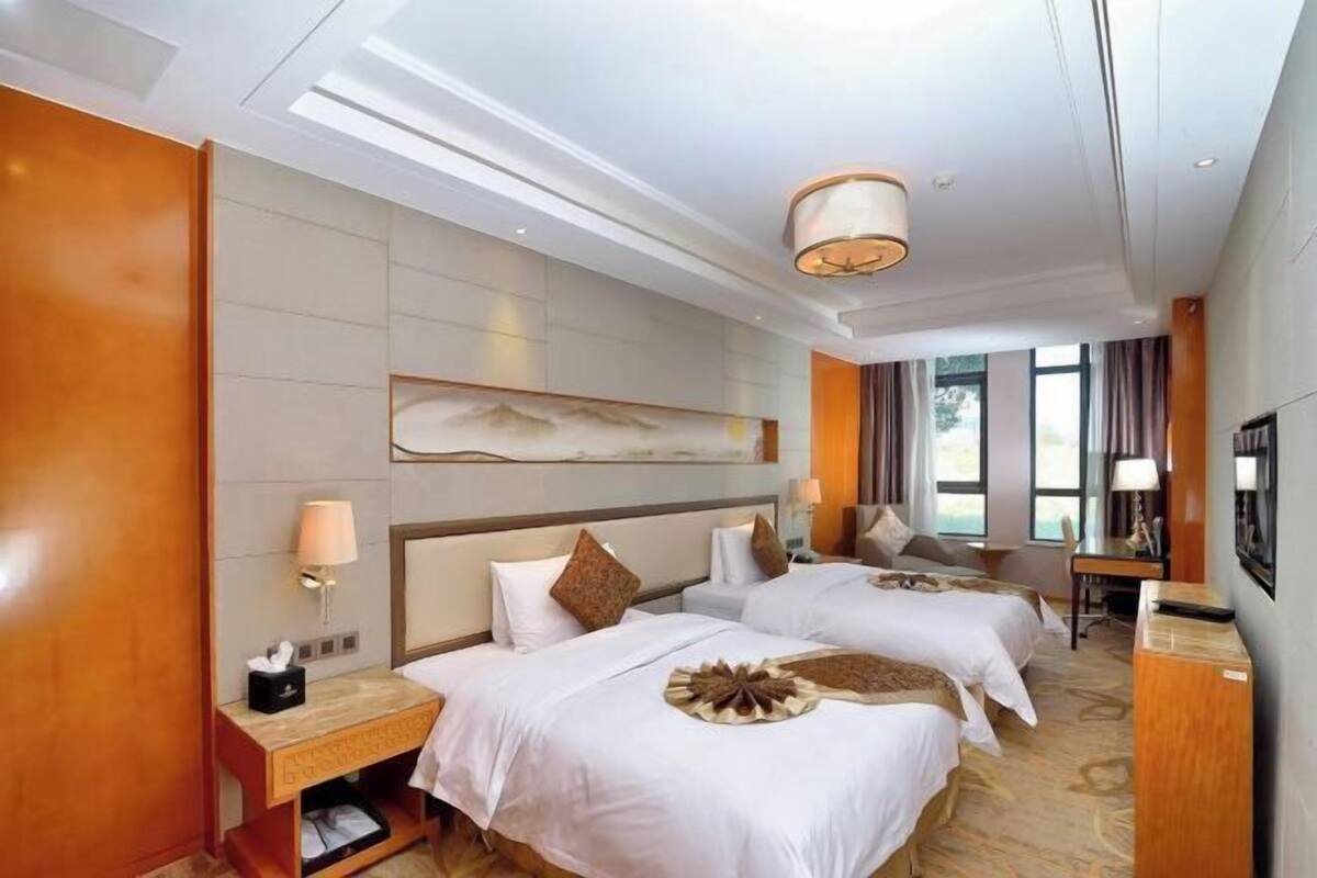 Une chambre d’hôtel avec deux lits, un bureau, une lampe, une télévision et une grande fenêtre.