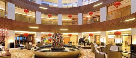 Un hall de hotel de varios niveles con una fuente central, zonas de estar y un diseño moderno.