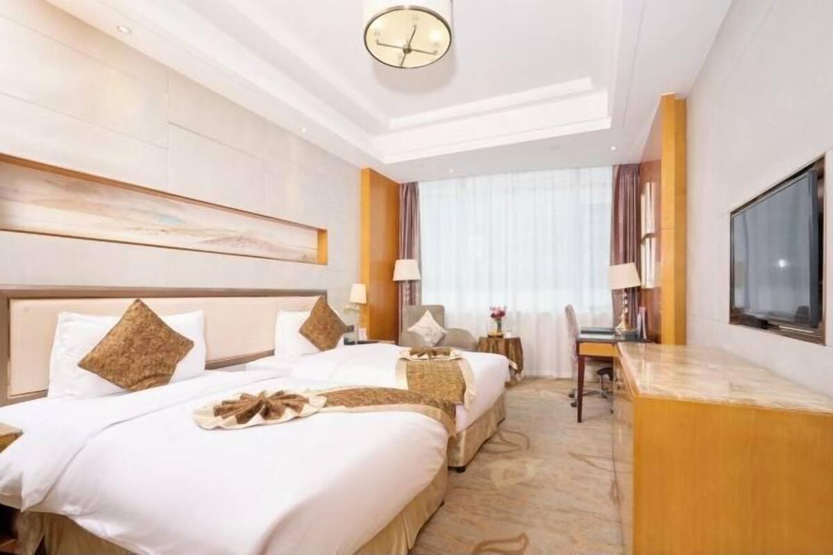 Une chambre d’hôtel avec deux lits, un bureau, une télévision et une grande fenêtre avec des rideaux.