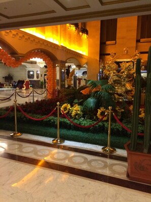 A lobby with a marble floor, a red carpeted area, and a decorative plant arrangement.