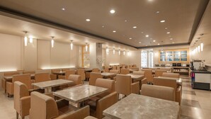 A spacious dining area with multiple tables and chairs, recessed lighting, and a kitchen area in the background. - Kindness Hotel Han Shen (Kaohsiung)