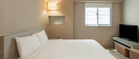 A hotel room with a large bed, a TV on a wooden stand, a window with blinds, and a bedside lamp.