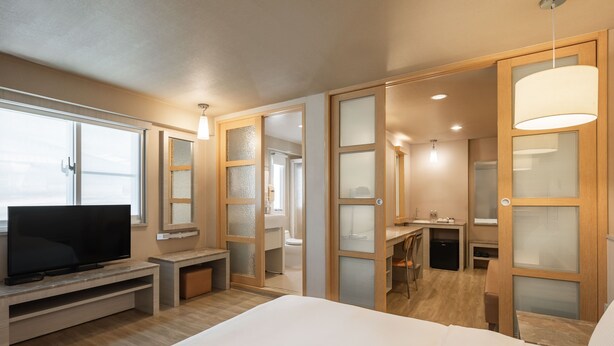 A modern hotel room with a large bed, a TV, a desk, and a bathroom visible through a glass partition. - Kindness Hotel Han Shen (Kaohsiung)