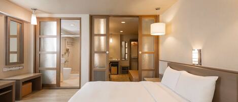 Ein Hotelzimmer mit einem großen Bett, einem Schreibtisch, einem Stuhl, einem Spiegel und einem durch eine offene Tür einsehbaren Badezimmer.