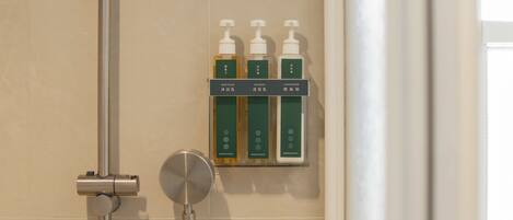 A bathroom with a shower, a hand dryer, and a shelf with three bottles of toiletries.