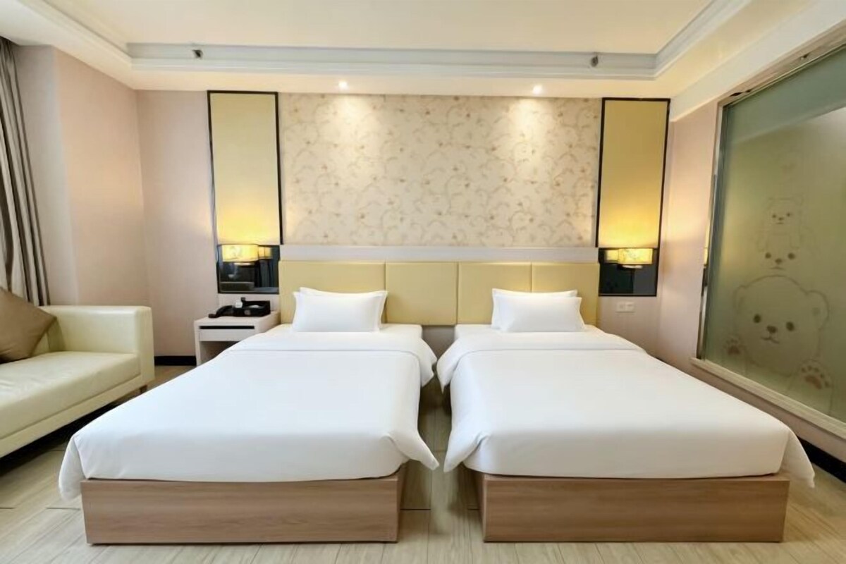 Habitació d'hotel amb dos llits, un sofà i una finestra gran amb vistes.