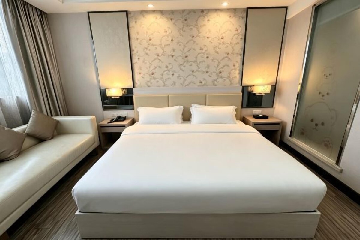 Habitació d'hotel amb un llit gran, un sofà, dues taules de nit i una finestra ampla.