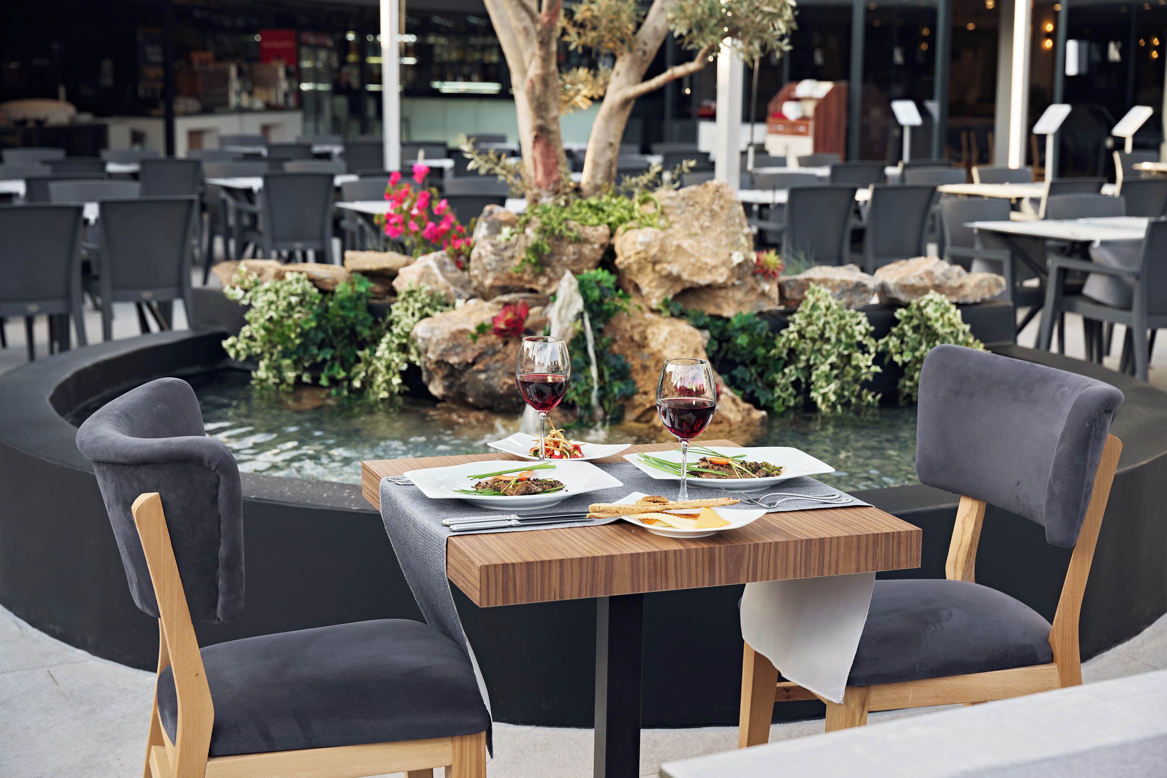 A dining table with two chairs, a small fountain, and a view of a restaurant area.