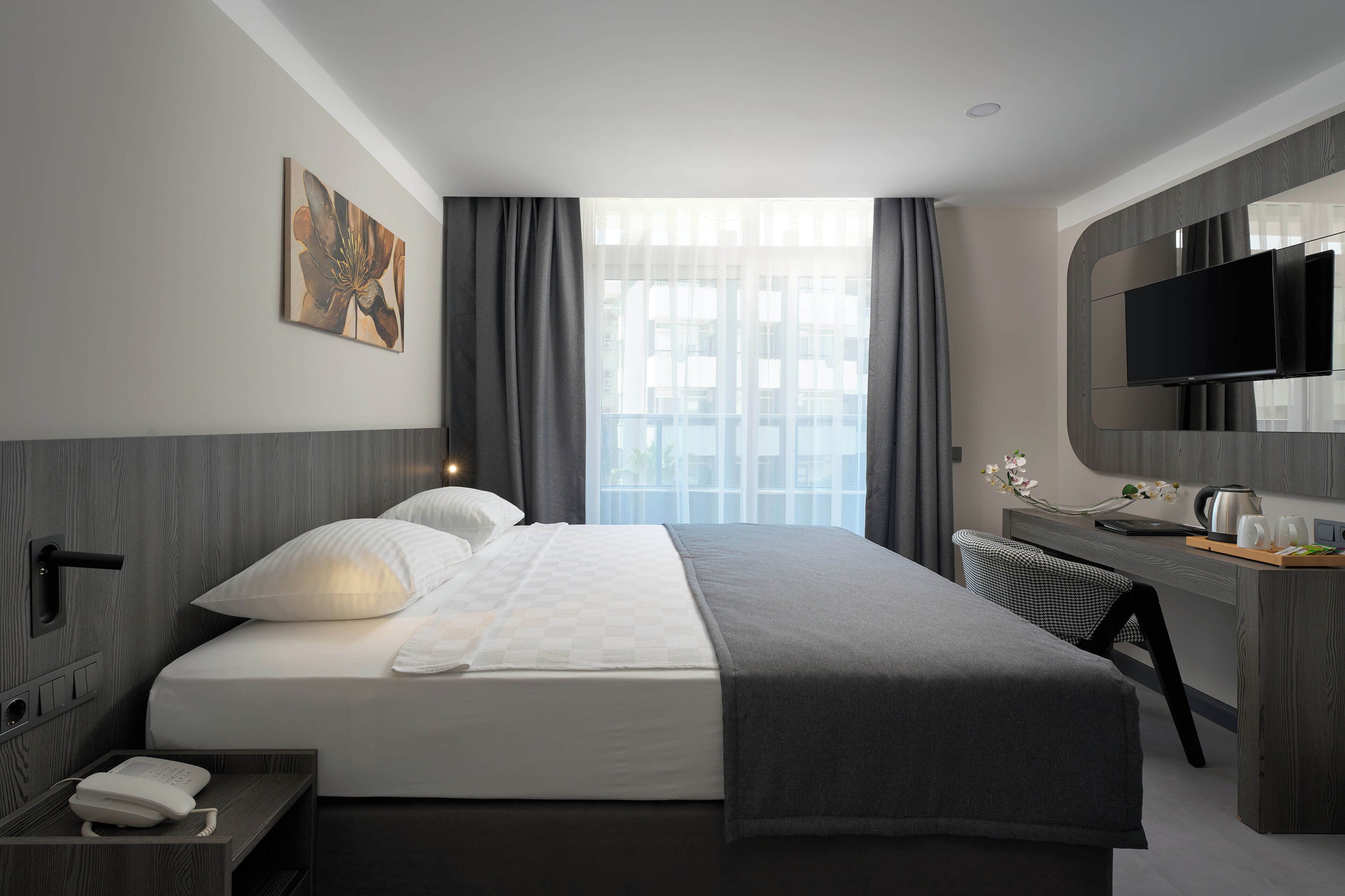 Camera d'albergo moderna con un ampio letto, una scrivania, una TV a schermo piatto e una finestra con tende.