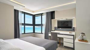 A modern hotel room with a large bed, a desk, a television, and a view of the ocean. - Krizantem Hotel - All Inclusive (Alanya)