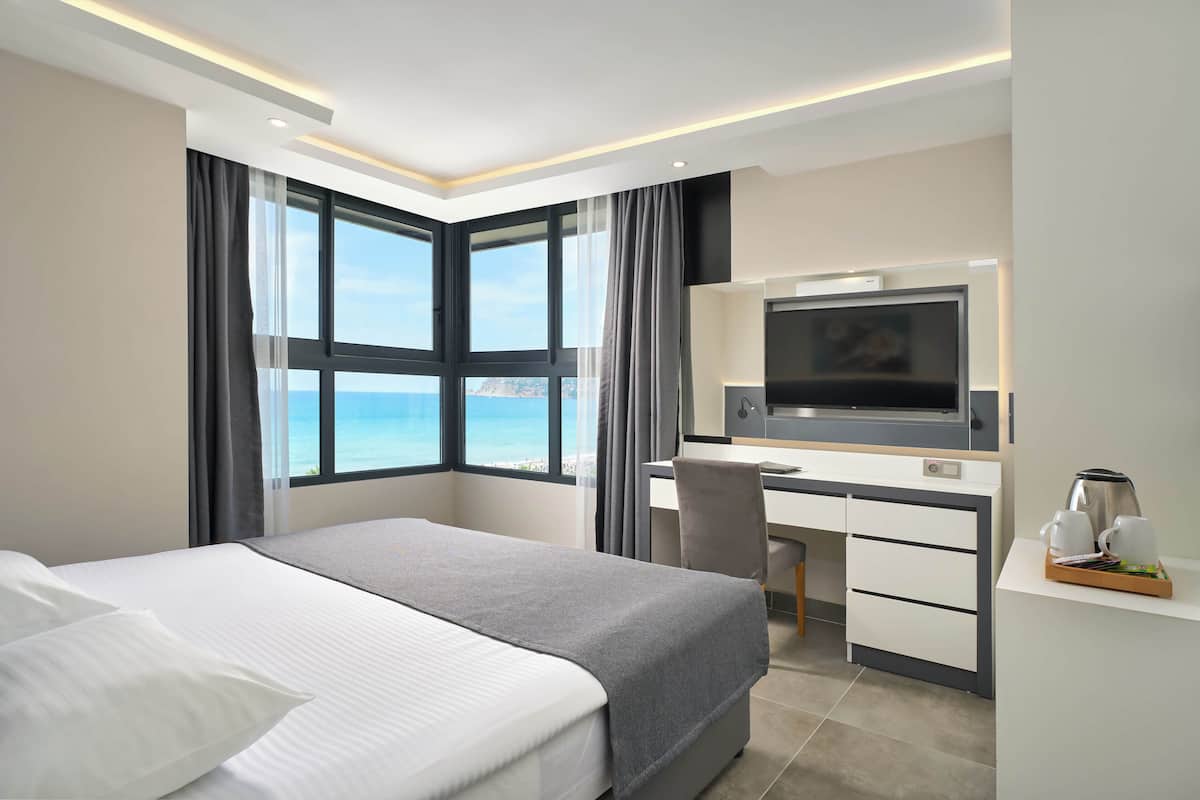 A modern hotel room with a large bed, a desk, a television, and a view of the ocean.