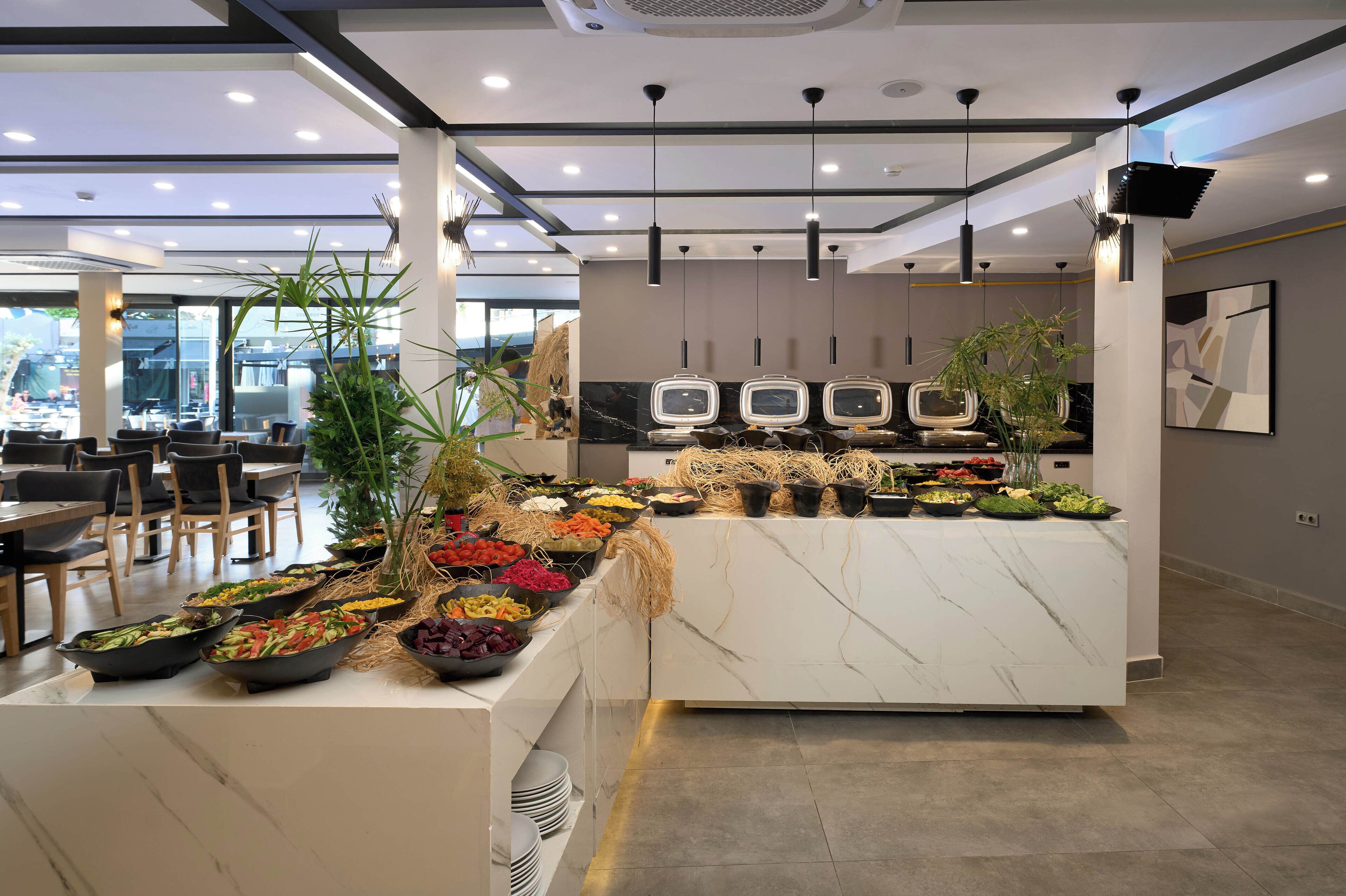 A modern buffet area with a variety of food options, including fruits, vegetables, and grains, arranged on a marble counter.