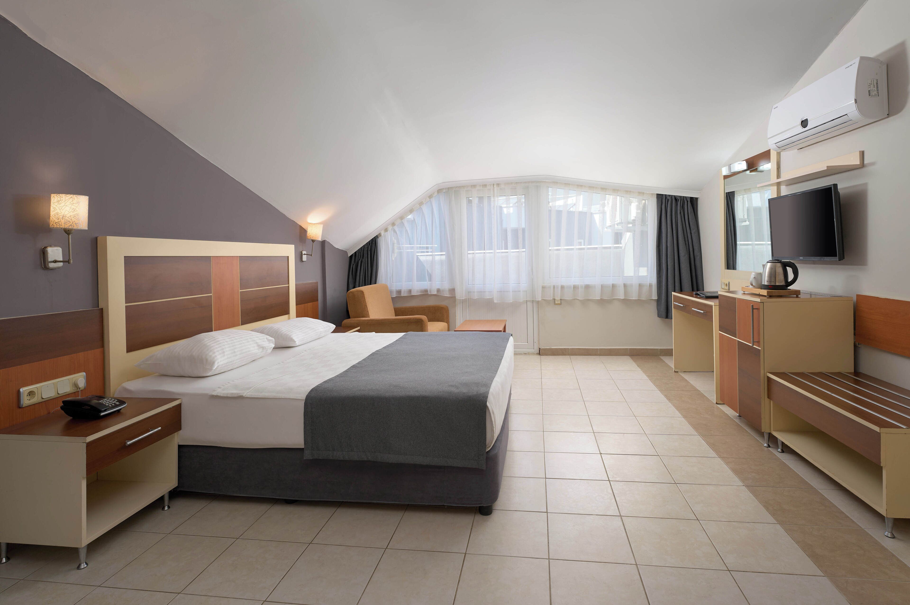 A hotel room with a large bed, a desk with a telephone, a chair, a TV, and a coffee maker.