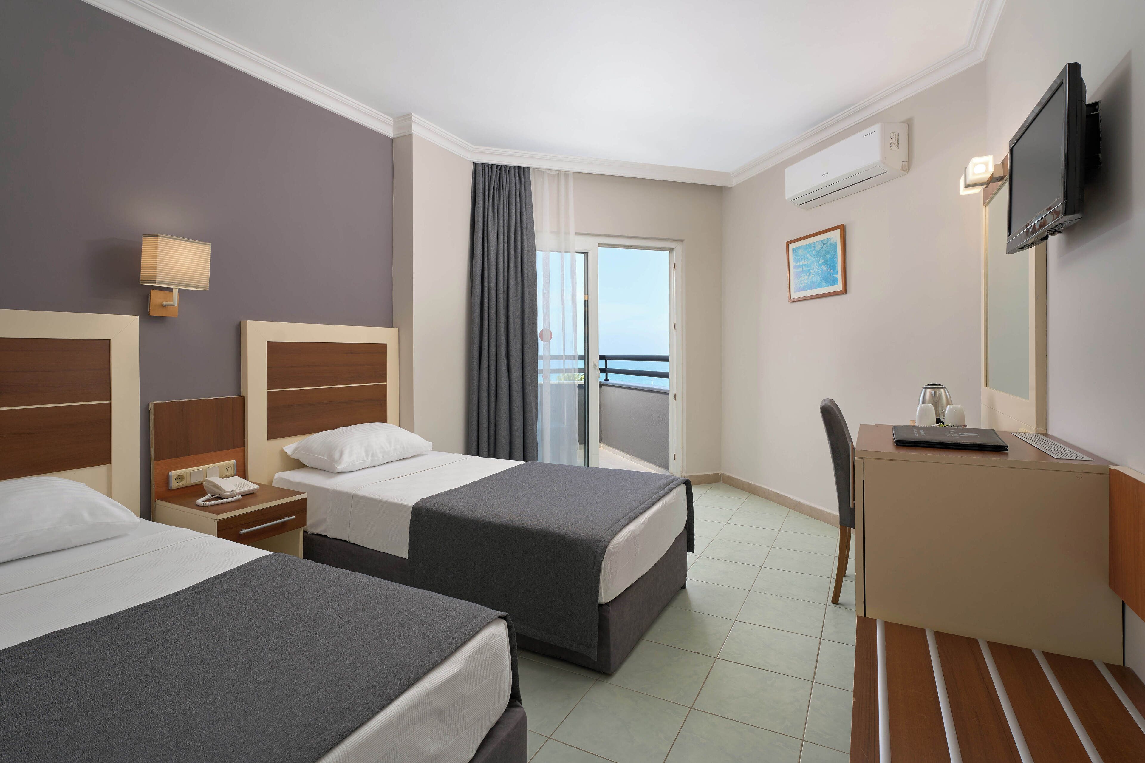 A hotel room with two beds, a desk, a chair, a TV, and a balcony.