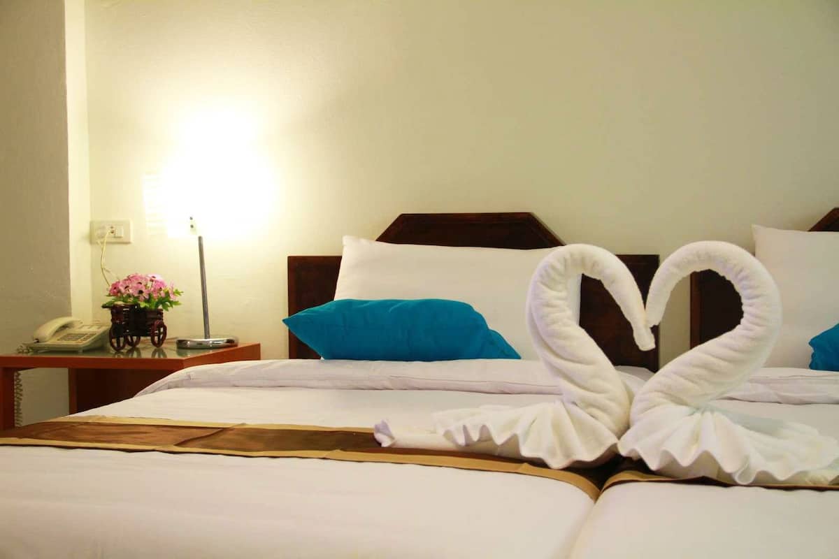 Een hotelkamer met een bed, voorzien van een handdoek in de vorm van een zwaan, een nachtkastje met een telefoon en een bloevas, en een lamp.