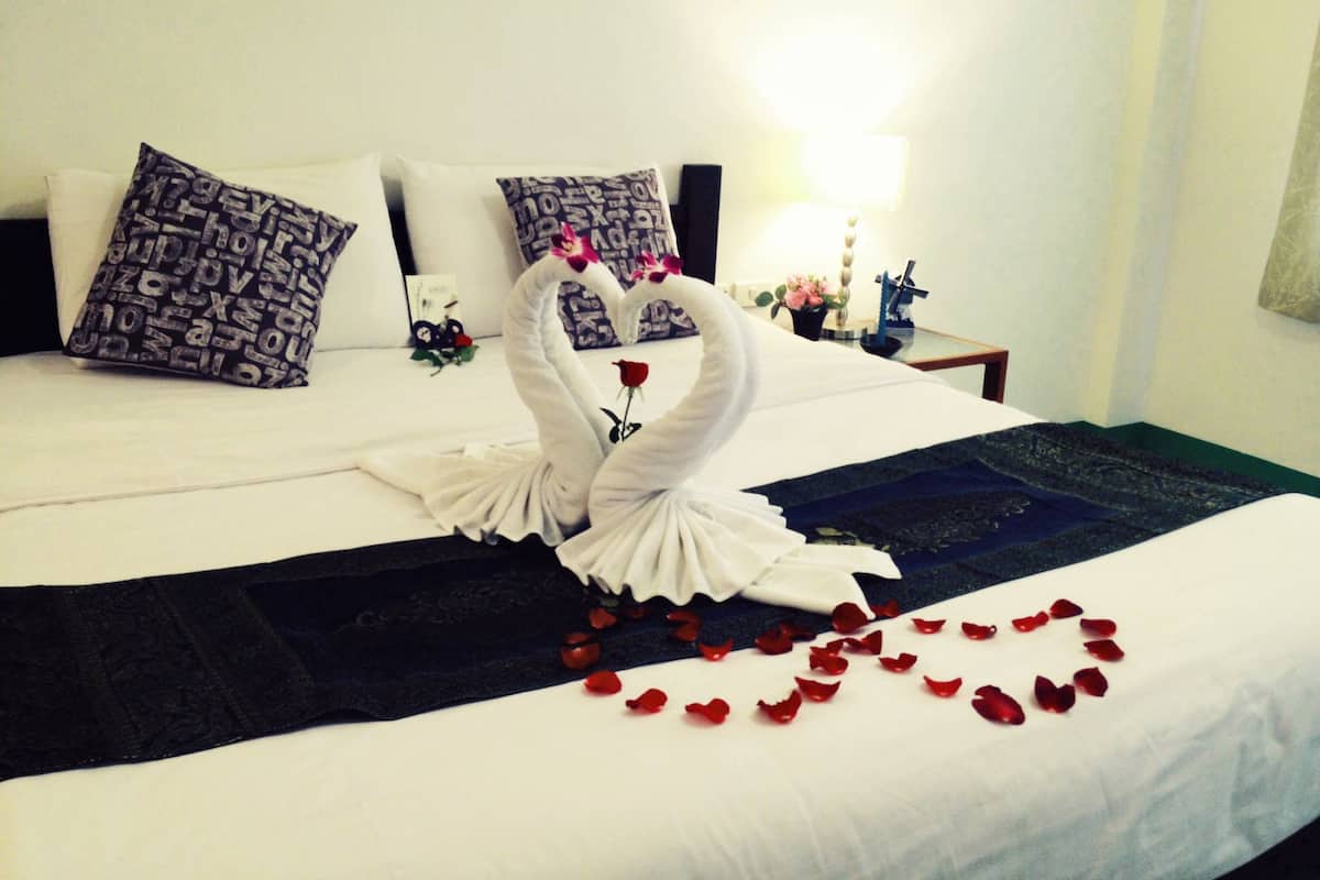 Een hotelkamer met een bed, versierd met een zwaan van handdoeken en rozenblaadjes op het beddegoed.