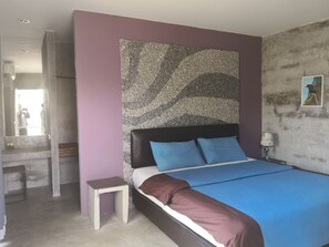 Ein Schlafzimmer mit Bett, kleinem Nachttisch, großem abstrakten Wandbild und einem gerahmten Bild an der Wand.