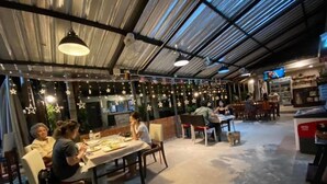 Ein Restaurant mit Tischen, Stühlen, Deckenbalken und hängenden Lampen.