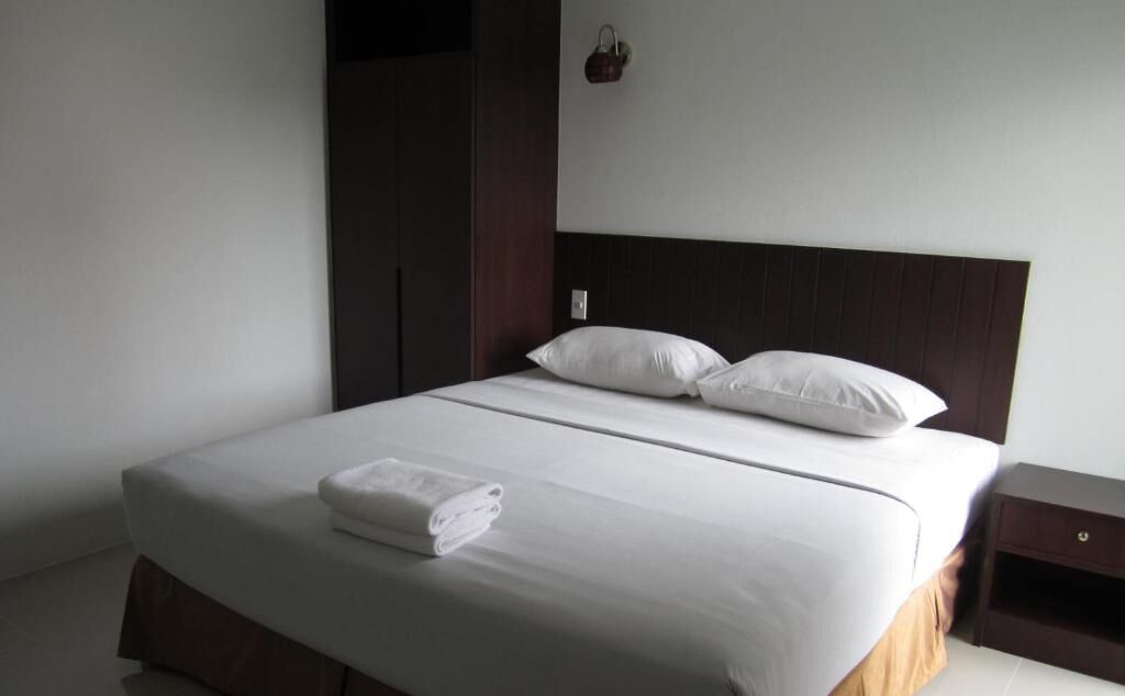 A neatly made bed with white linens and pillows, a wooden nightstand with a drawer, and a dark wooden wardrobe.