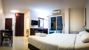Une chambre d’hôtel comprenant un lit, un bureau, une chaise, une télévision, une armoire et une salle de bain, le tout visible à travers une porte ouverte.