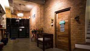 Un couloir aux murs de briques, avec un banc en bois, un vélo et une porte sur laquelle on peut lire : « SHACKE'S BAR ».