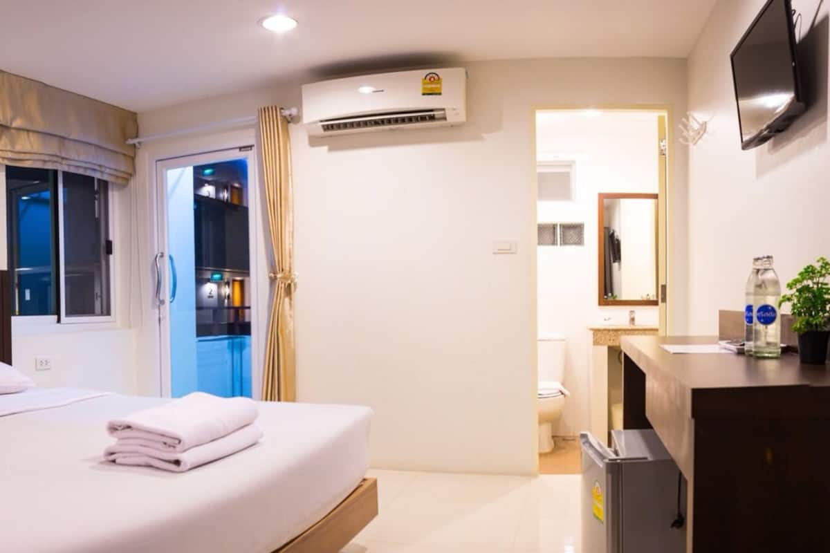 Une chambre d’hôtel avec un lit, un bureau, un climatiseur, une télévision et une salle de bain visible à travers une porte ouverte.