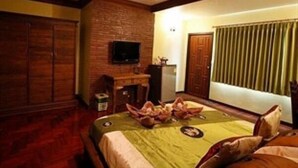 A hotel room with a brick wall, a television mounted on the wall, a desk with a chair, and a bed with a green bedspread. - Baan Fern Talay (Cha-am)