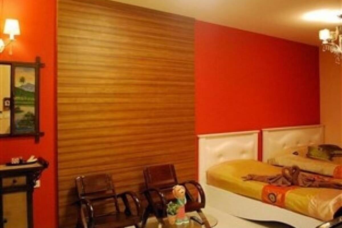 Una habitación de hotel con cabecera de madera, una cama con manta amarilla, dos sillas, una mesita y una lámpara de pared.