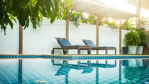 Una piscina con dos sillones de descanso y plantas en macetas.
