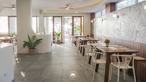 Un restaurante moderno con techos altos, amplias ventanas y una pared de mármol. Las mesas están dispuestas para comer, y hay plantas en macetas.