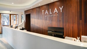 Un mostrador de recepción moderno con un panel de pared de madera y el nombre "TALAY HOTEL & VILLAGE" bien visible.