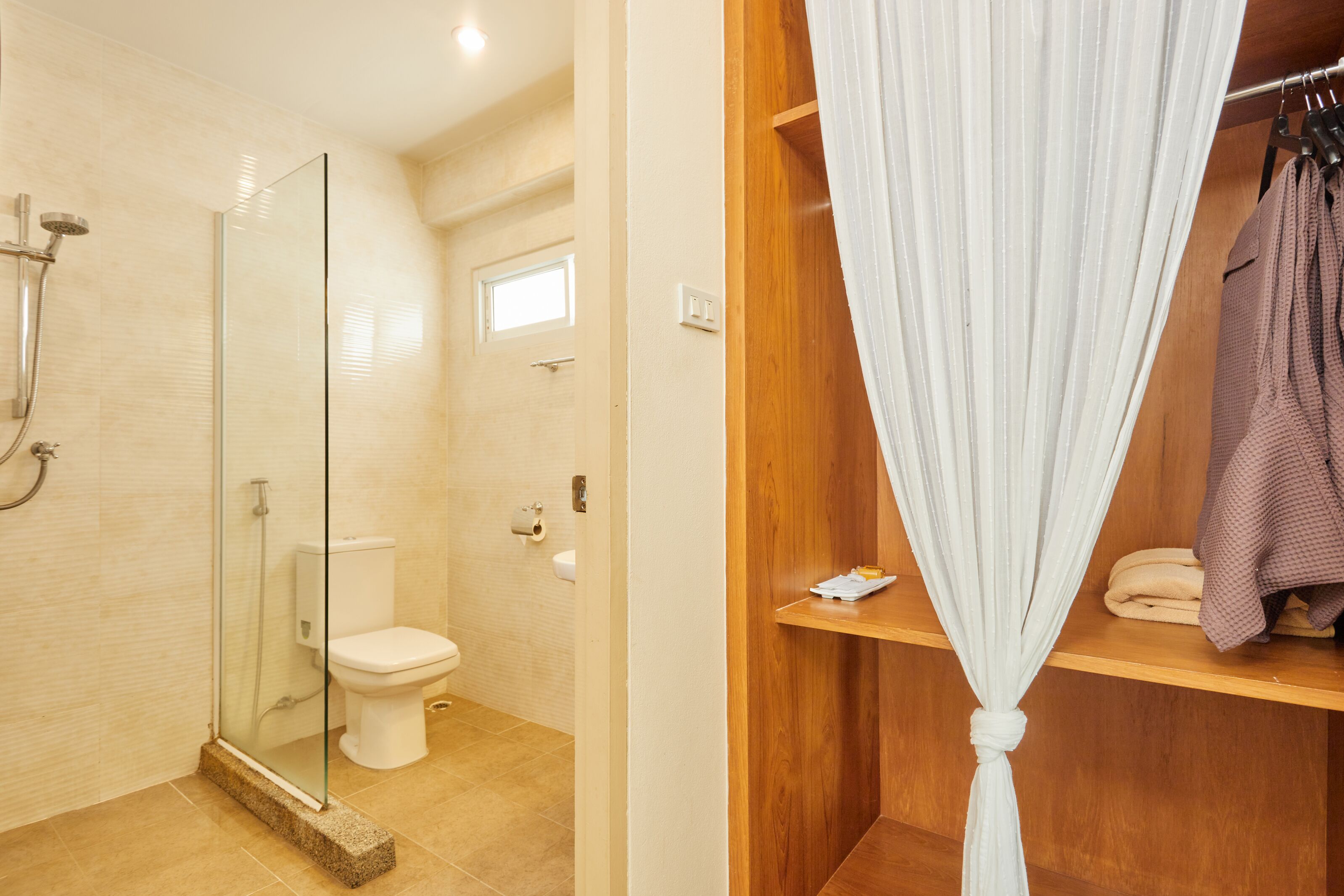 Un baño con ducha envuelta en vidrio, inodoro y tocador de madera con cortina.