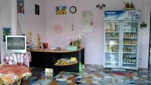 A room with a tiled floor, a refrigerator stocked with beverages, a television, and a desk with various items.