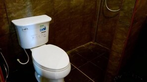 Des toilettes blanches dotées d’un panneau de commande, dans une salle de bain aux murs recouverts de carreaux foncés.