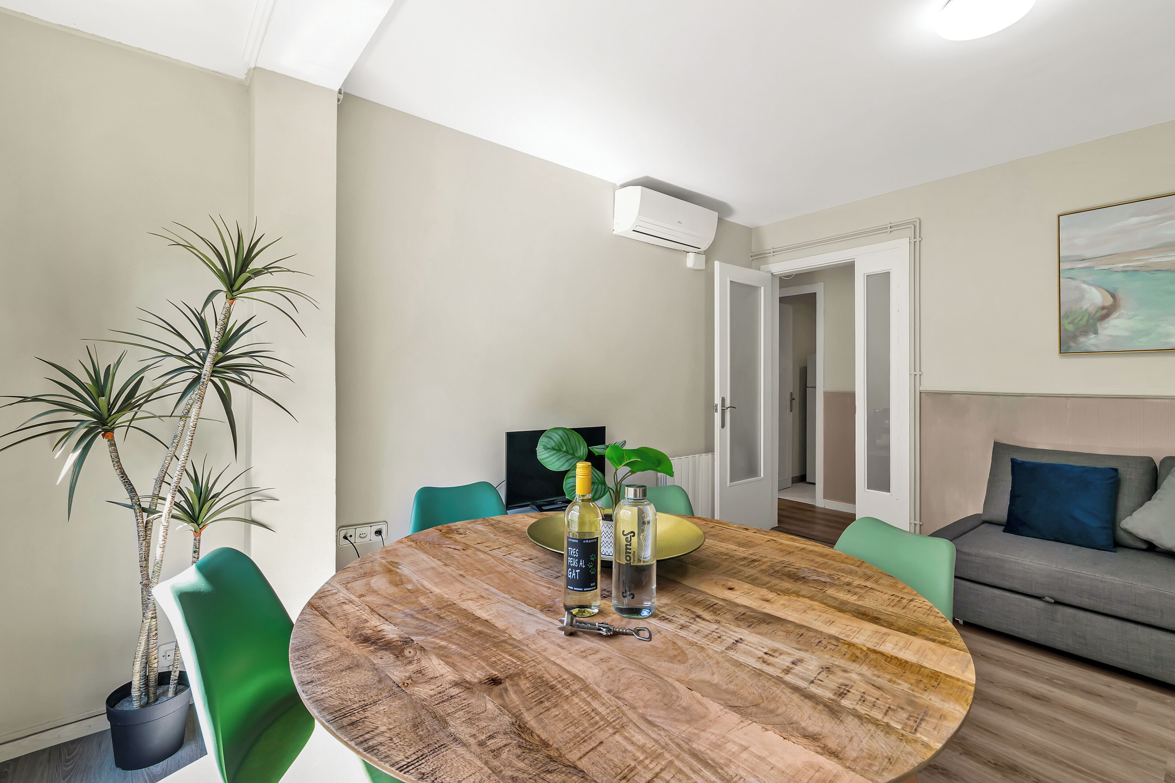 Ein modernes Wohnzimmer mit einem runden Holztisch, grünen Sesseln, einem grauen Sofa und einem Blumentopf.