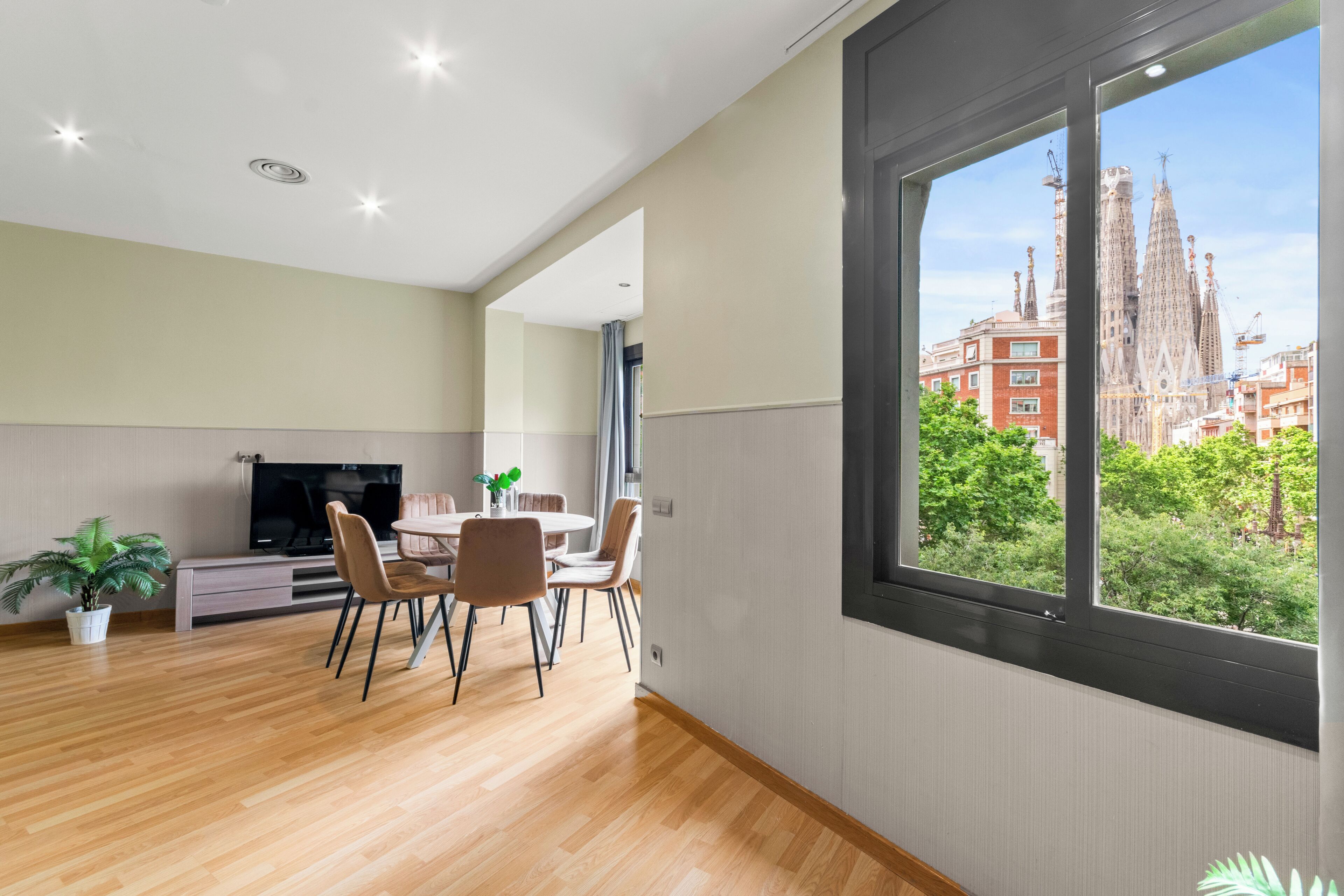 A modern living room with a dining area, a TV, and a large window with a view of a historic building.