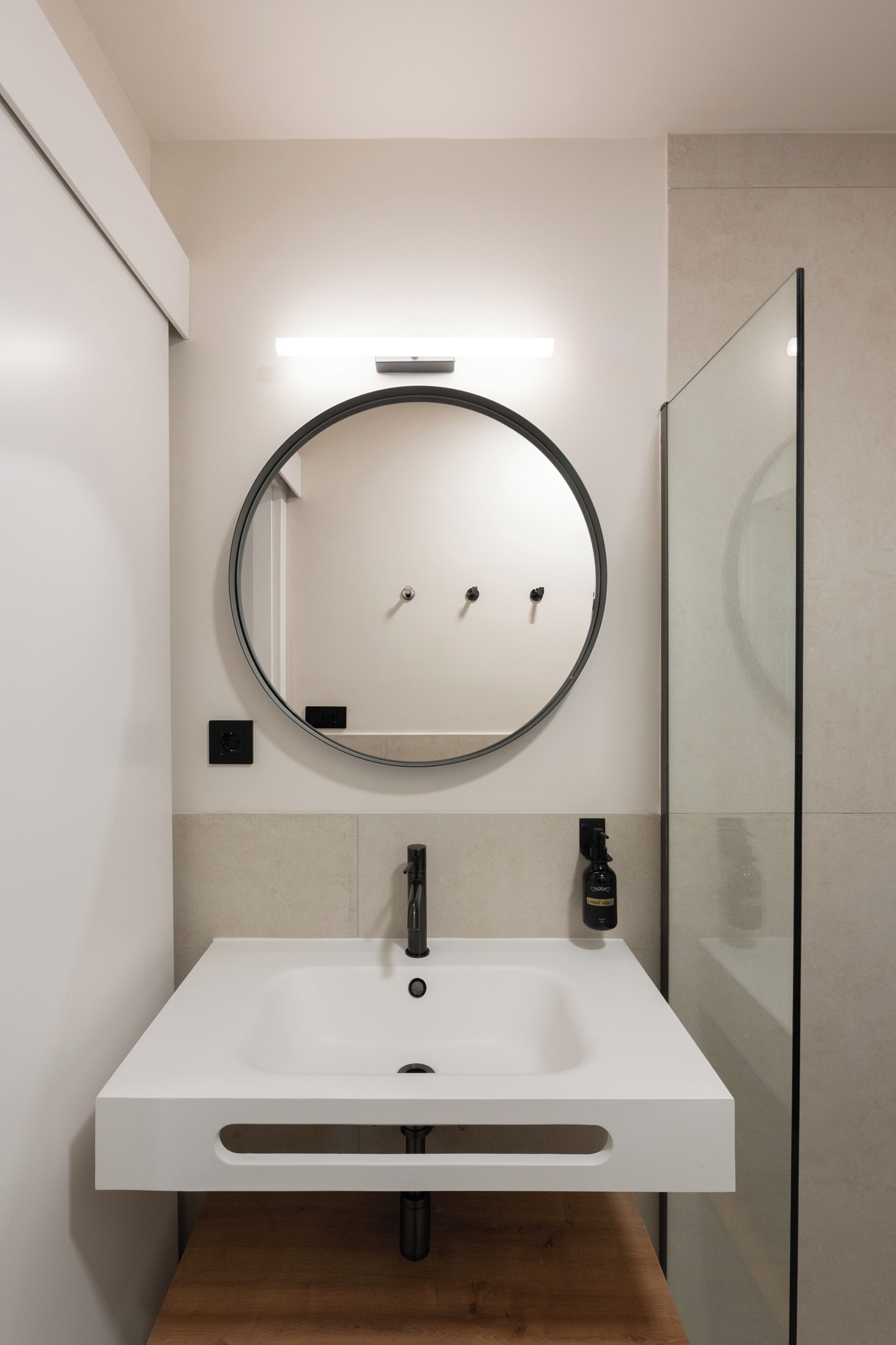 A modern bathroom with a round mirror, white sink, and a glass shower enclosure.