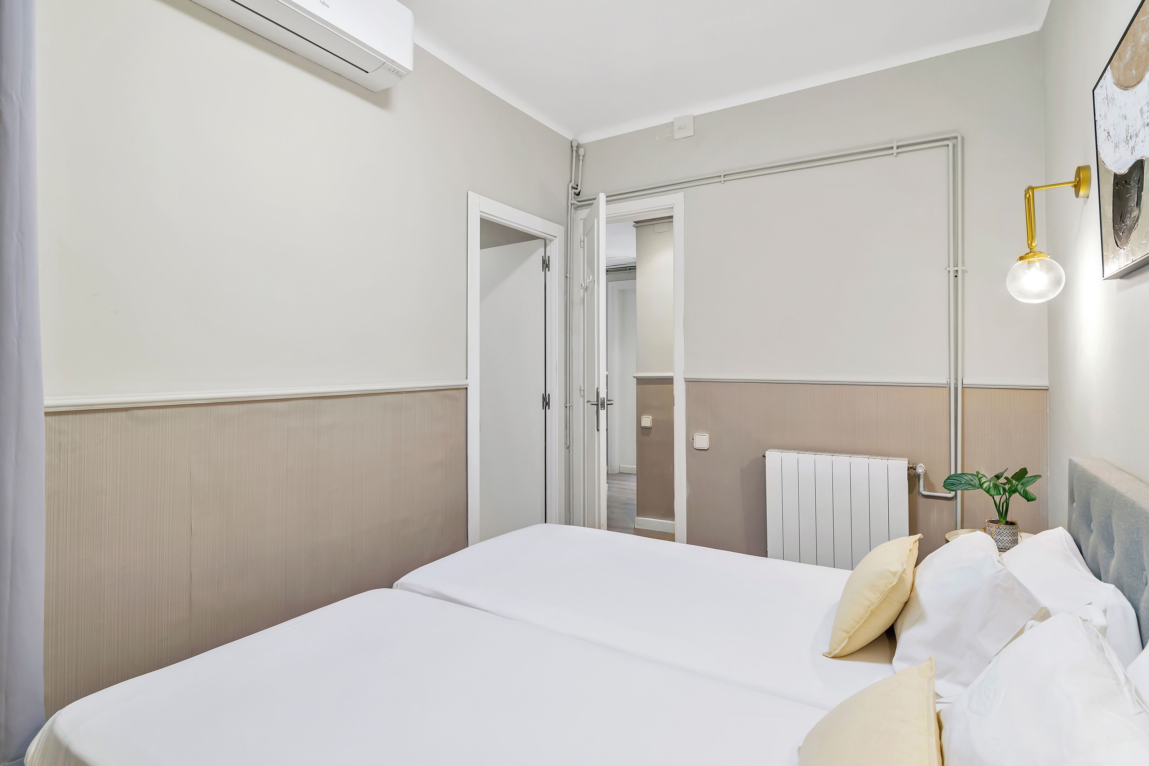 Een hotelkamer met een bed, een nachtkastje met een lamp, een potplant en een spiegel aan de muur.