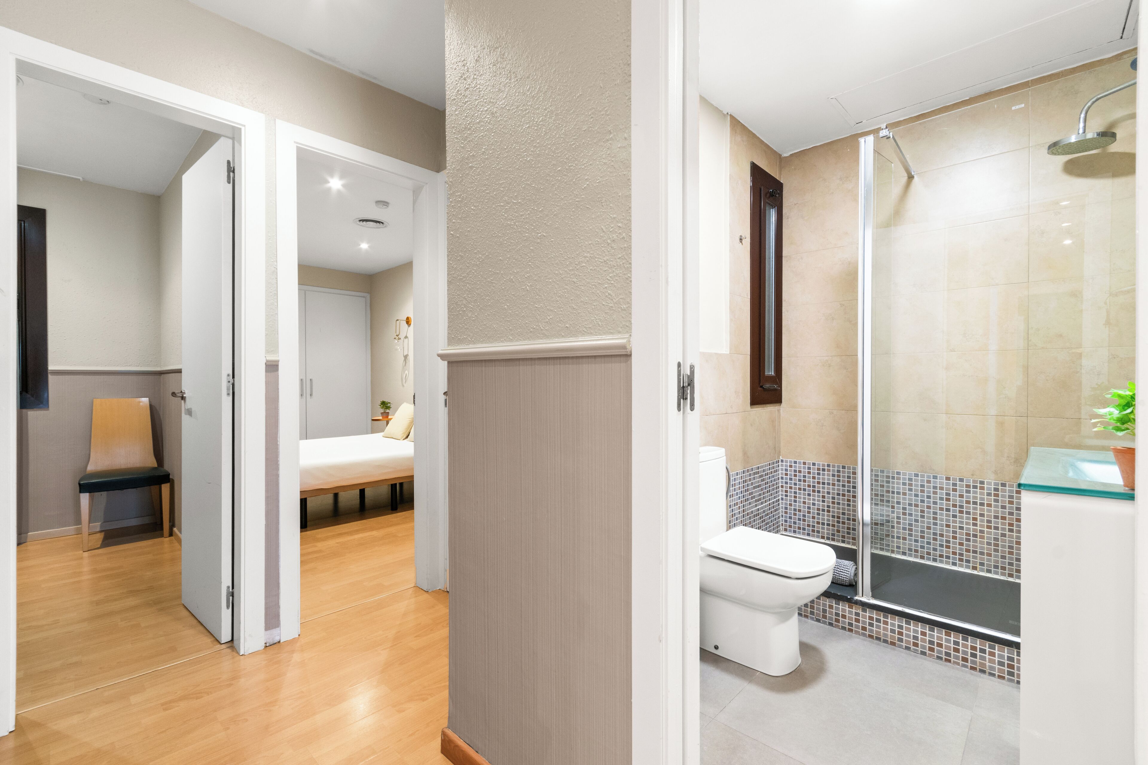 A modern bathroom with a glass shower enclosure, a toilet, and a bench in a hallway.