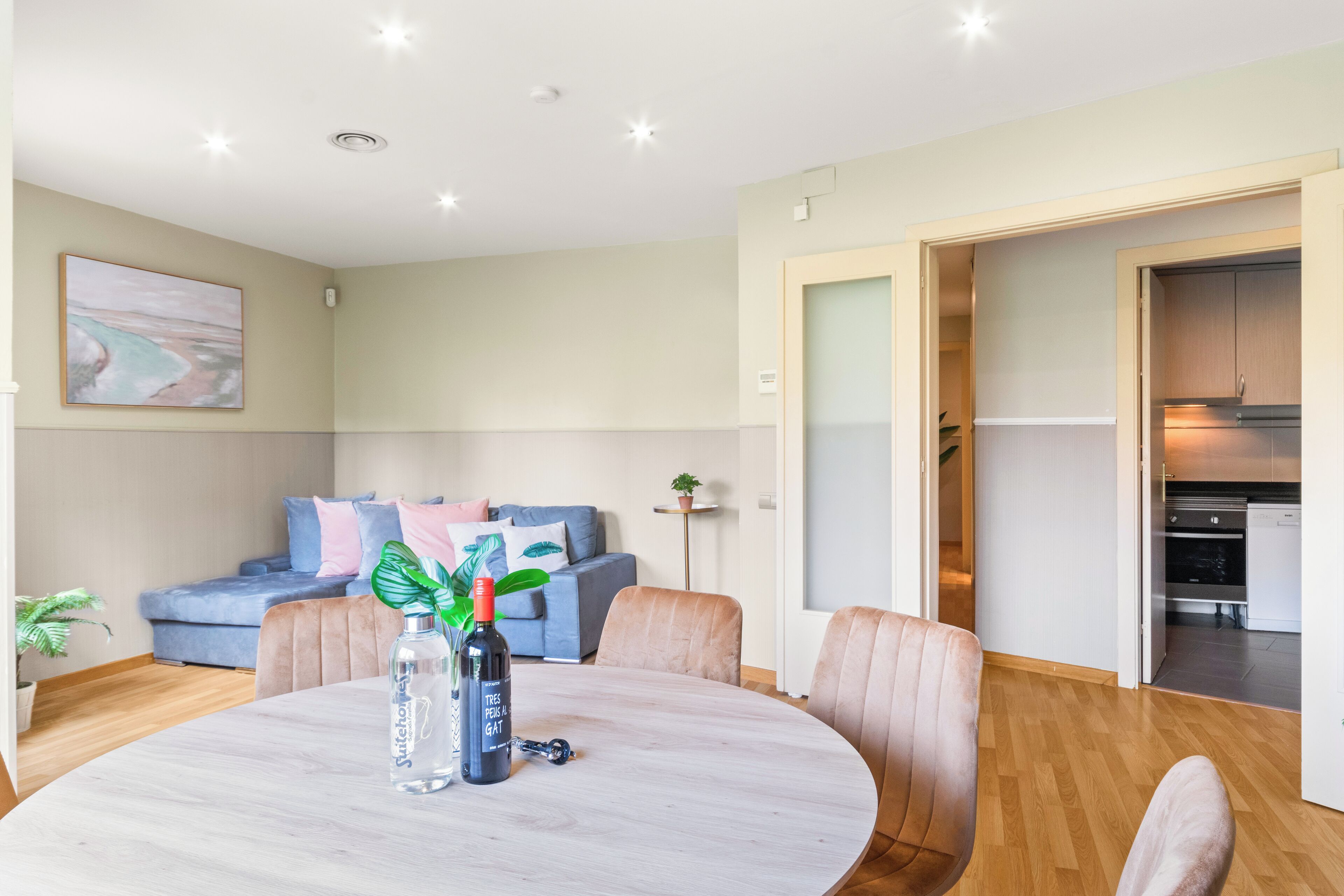 Een moderne woonkamer met een ronde tafel, een bank en een keuken die door een open deur zichtbaar is.