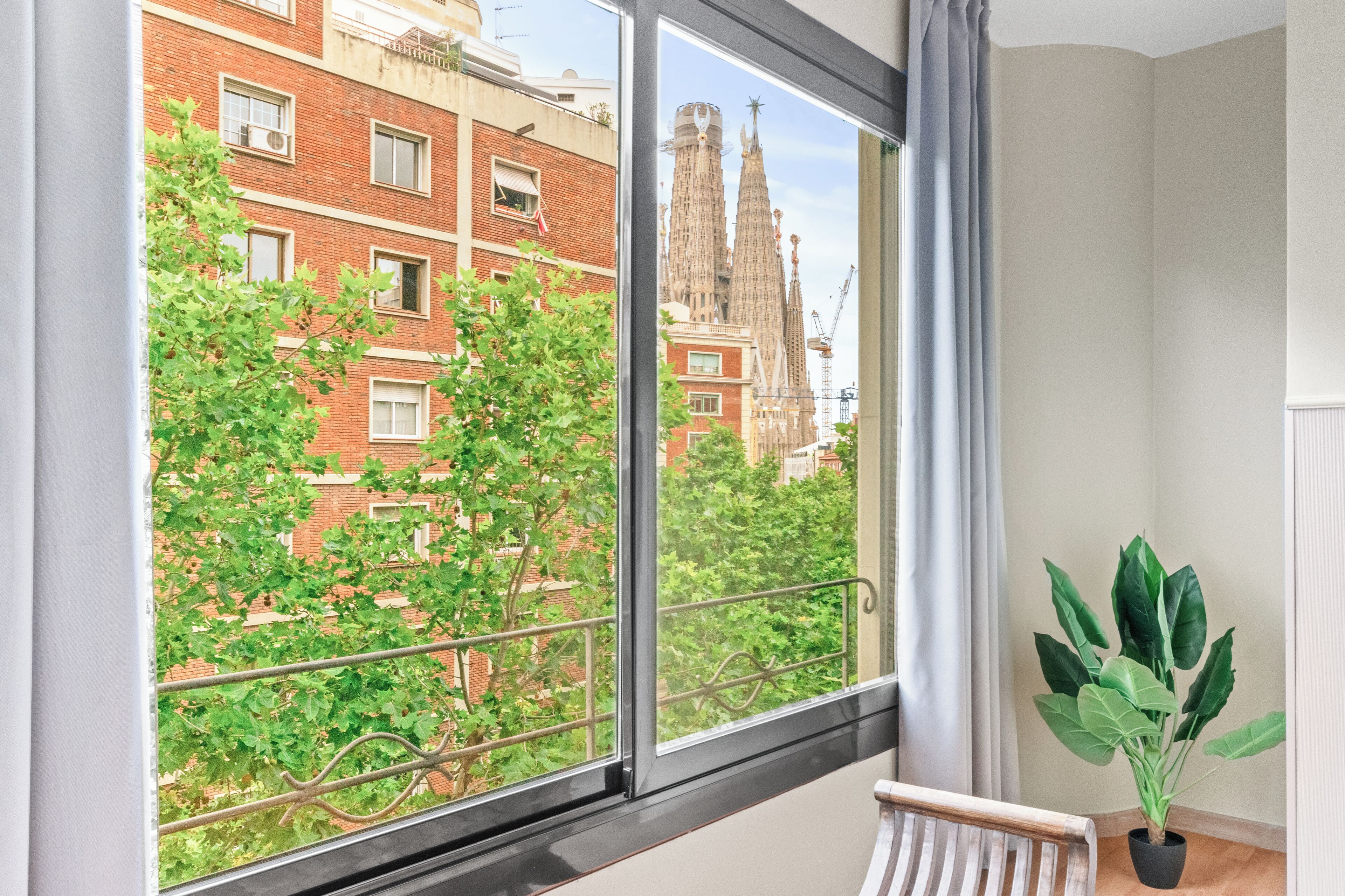 Ein Zimmer mit großem Fenster und Blick auf eine Stadtlandschaft, darunter ein markantes Gebäude mit zwei Türmen.